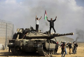 Palestinians wave their national flag and celebrate by a destroyed Israeli tank at the southern Gaza Strip fence east of Khan Younis on Saturday, Oct. 7, 2023. Thousands of Hamas-led militants stormed across the border into Israel, killing 1,200 people, mostly civilians, and taking roughly 250 captive, according to Israeli authorities. (AP Photo/Yousef Masoud, File)