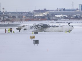 Investigators inspect the scene on the tarmac of Pearson International Airport on Tuesday, Feb. 18, 2025, after Delta Air Lines Flight 4819 crashed upon landing from Minneapolis one day earlier. JACK BOLAND/TORONTO SUN