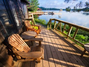 Muskoka chairs sitting on a wooden porch facing a quiet lake are depicted in this file photo.