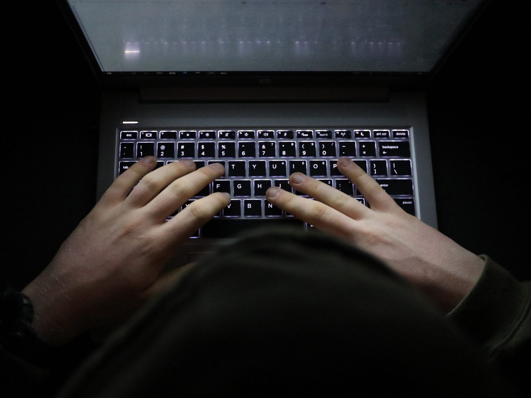 A simple, very dark image of hands typing on a backlit keyboard at night.