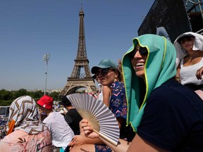 Stephanie Touissaint, foreground, uses a fan to keep cool in the sweltering heat at Eiffel Tower Stadium during a beach volleyball match between Cuba and Brazil at the 2024 Summer Olympics, July 30, 2024, in Paris.