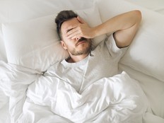 Tired young man in bed closing his eyes before waking up. Hangover morning. Sleep disorder and problems.