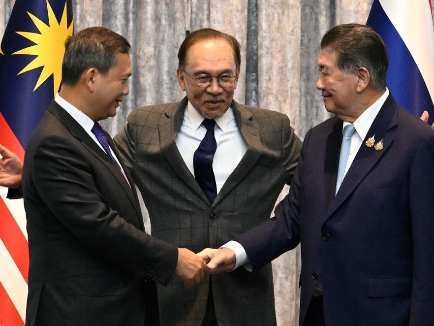 Cambodia's Prime Minister Hun Manet (L) and Thailand's acting Prime Minister Phumtham Wechayachai (R) shake hands as Malaysia's Prime Minister Anwar Ibrahim (C) puts his arms around them following a press conference after talks on a possible ceasefire between Thailand and Cambodia in Putrajaya on July 28, 2025. Thailand and Cambodia began discussing a ceasefire in their festering border dispute on July 28, as the deadly skirmish dragged into a fifth day. (Photo by MOHD RASFAN / POOL / AFP)