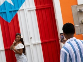 A man photographs a woman in front of a Puerto Rican flag mural in Old San Juan, Puerto Rico on May 13, 2025. (Ricardo ARDUENGO/AFP)