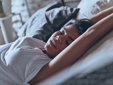 Woman dreaming with arms above her head, sleeping alone in bed.
