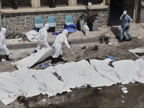 Morgue workers place bodies into bags.