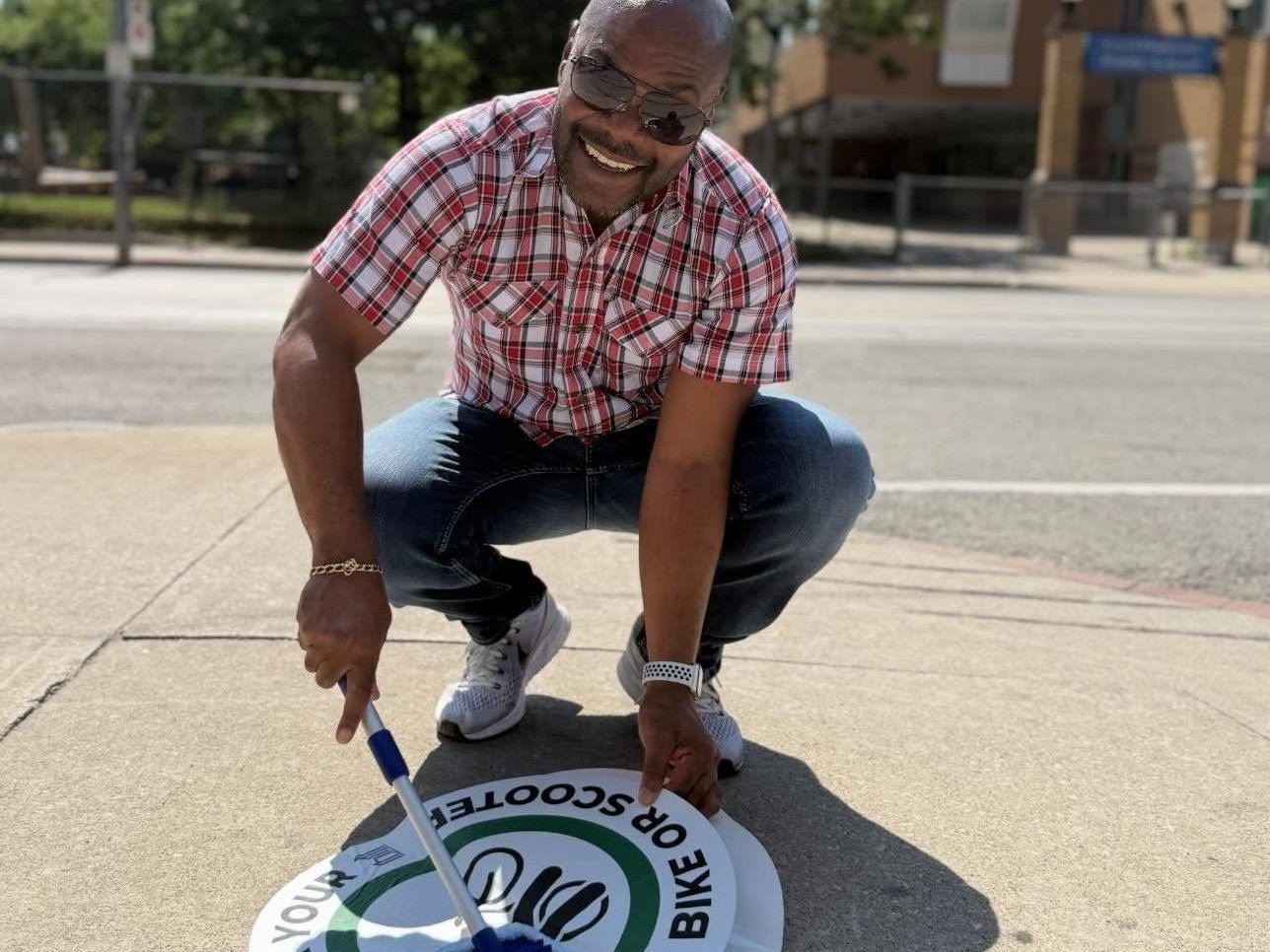 Councillor Chris Moise installs a “walk your bike” decal on a sidewalk in his Toronto Centre ward.