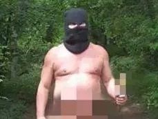 Naked man (private area blurred out) wearing balaclava and clogs while holding stick in woods near castle in Slovakia.