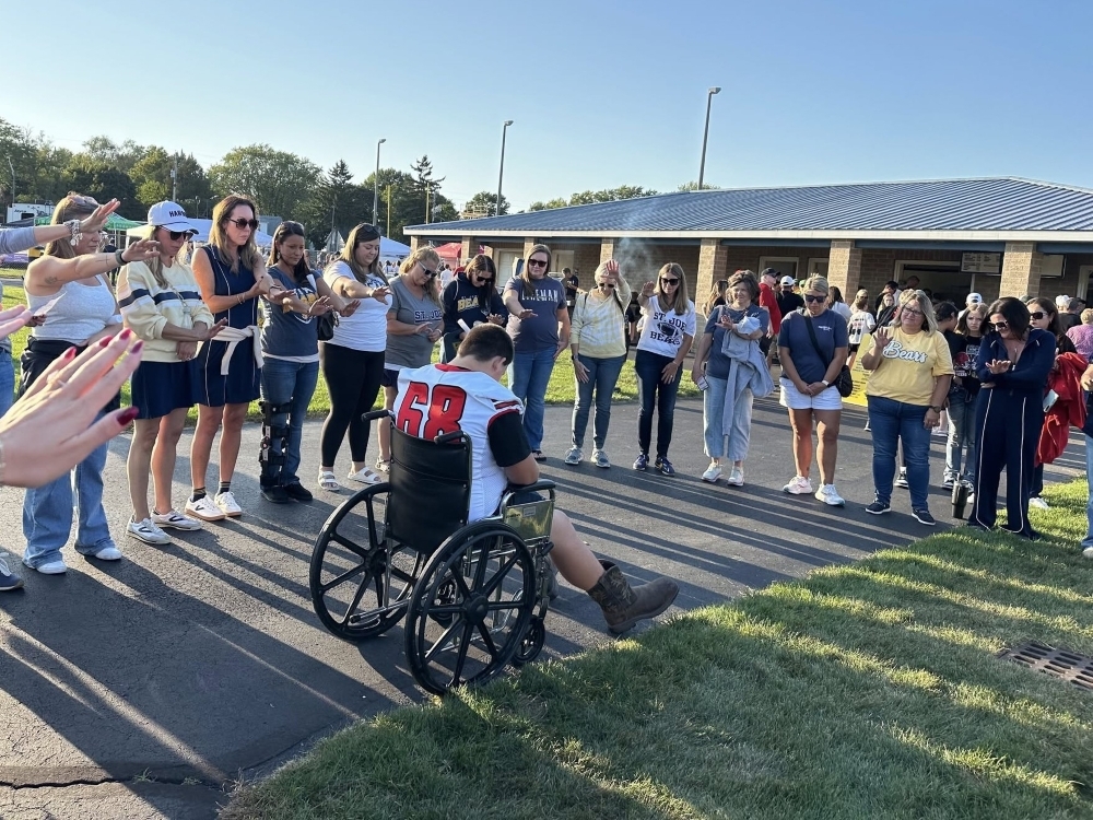 Michigan high school football player Colton Mims is pushed in a wheelchair before a game.