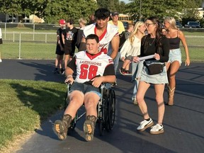 Michigan high school football player Colton Mims is pushed in a wheelchair before a game.