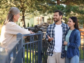 Friendly relationship with neighbours. Happy young couple talking to senior woman near fence outdoors