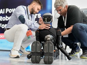 Spiros Makris, right, and Ioannis Karampinas technicians of Acumino replace a battery at the Booster T1 robot during the first International Humanoid Olympiad at the Olympic Academy, in ancient Olympia, Greece, Monday, Sept. 1, 2025.