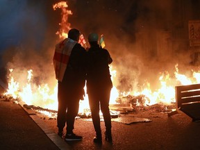 Demonstrators with Georgian and Ukrainian national flags are behind a burning barricade.
