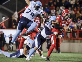 Argonauts' Derek Parish (centre) tackles Stampeders defenseman Vernon Adams Jr. during the second half of a CFL game in Calgary, Saturday, Oct. 18, 2025.