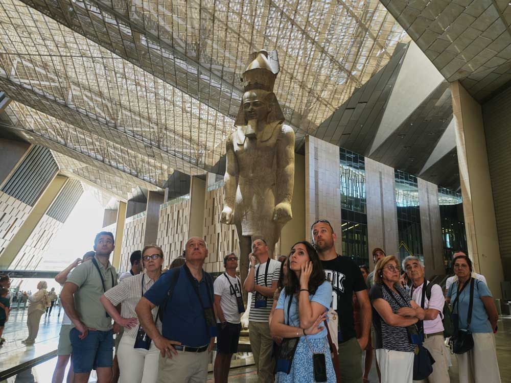 Tourists stand under a statue of Pharaoh Ramses II at the Grand Egyptian Museum in Giza, Egypt, Friday, May 23, 2025.