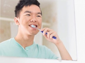 A teenager brushes his teeth in front of a mirror as part of his morning routine.