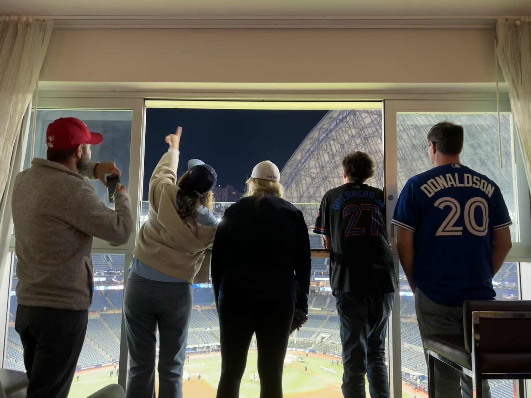 Five fans standing by window of room at Toronto Marriott City Centre Hotel looking at view of Rogers Centre and the open roof. (Supplied/Jenn Barbosa)  Five fans standing by window of room at Toronto Marriott City Centre Hotel looking at view of Rogers Centre and the open roof. (Supplied/Jenn Barbosa)