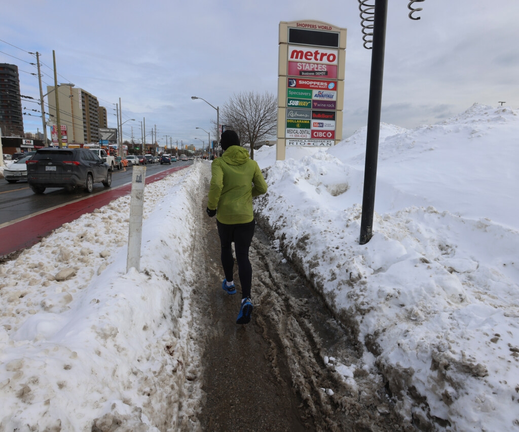  A jogger is cut off from the sidewalk and mountainous snow piles and heads into the icy bike path heading east along the Danforth to Victoria Park Aves. on Thursday February 20, 2025.