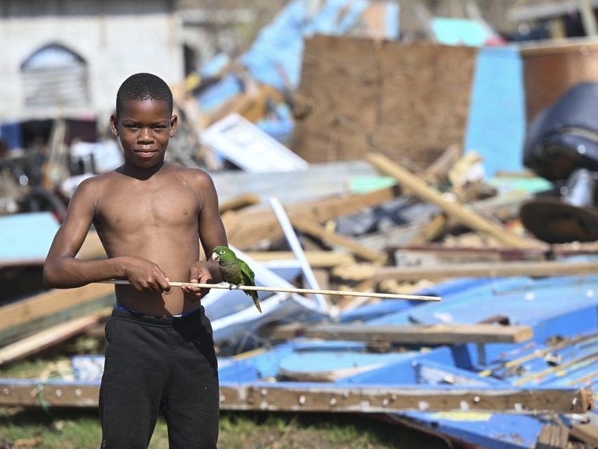Deano Morris poses with her pet parrot in front of damaged property after Hurricane Melissa in Bluefields, Westmoreland, Jamaica, October 31, 2025. 