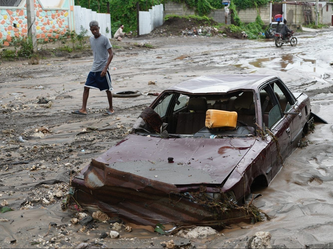 A pedestrian looks at a flooded car.