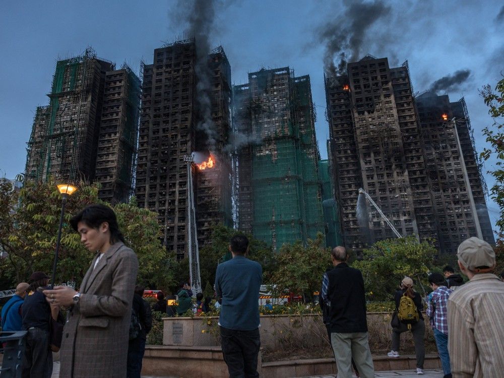 People watch as smoke rises from apartment buildings after a major fire swept through several blocks at the Wang Fuk Court residential estate in Hong Kong's Tai Po district, Thursday, Nov. 27, 2025.