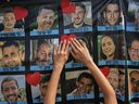 Hands place a heart-shaped sticker on a banner with photographs of Israeli hostages during a gathering in a square known as Hostage Square in Tel Aviv, Israel, Monday, October 13, 2025.