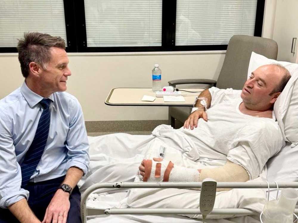 This handout photo taken and received from the NSW Premier's Department on Dec. 15, 2025 shows New South Wales Premier Chris Minns (left) talking with Ahmed Al Ahmed, the man who tackled and disarmed one of the Bondi Beach attackers, at St. George Hospital in Sydney.
