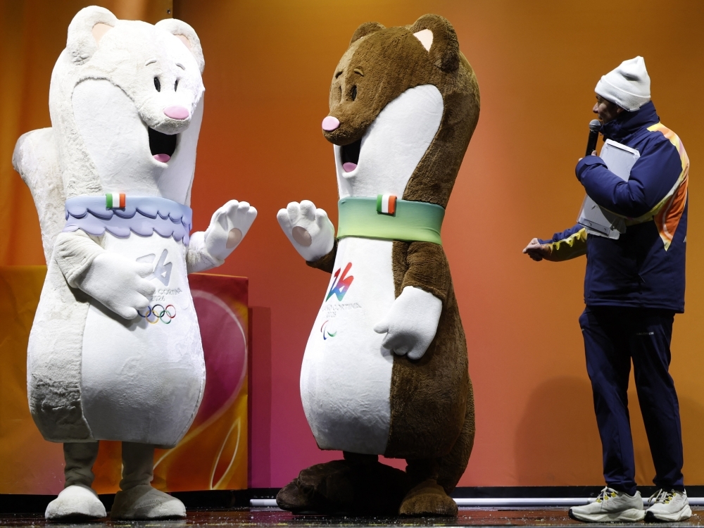 Tina (left) and Milo , the mascots of the Milano Cortina Olympic and Paralympic Games, stand on stage in Cortina d'Ampezzo before a torch relay event.