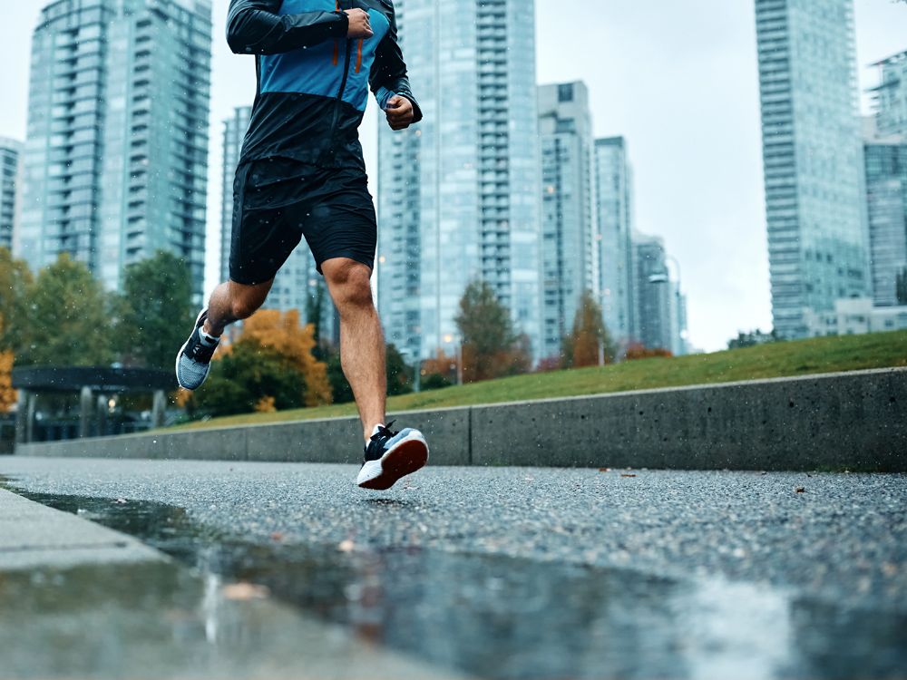 Unrecognizable athletic man running during rainy day.