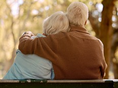 Back of older couple hugging on park bench.