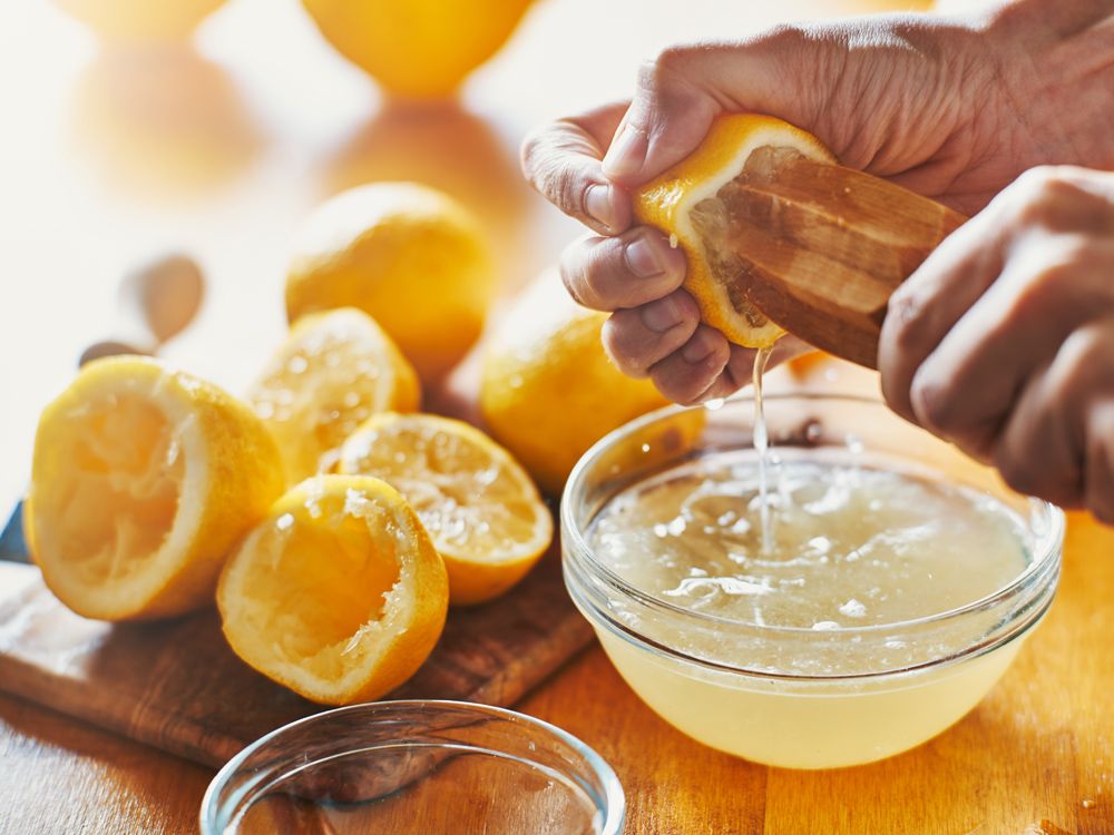 woman's hand squeezing juice from a lemon with wooden tool