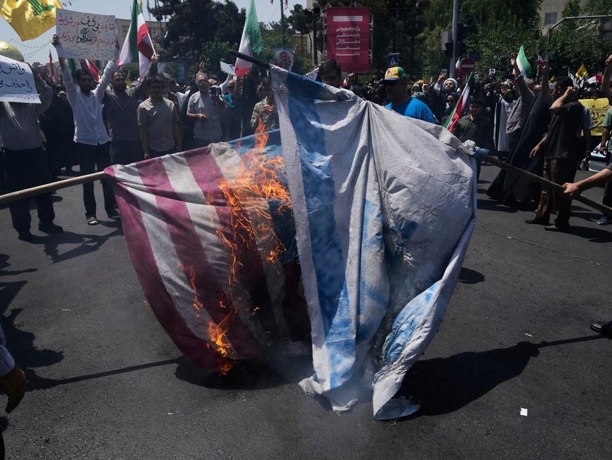  FILE – Iranian protestors burn representations of the Israeli and U.S. flags during a protest to condemn Israeli attacks on multiple cities across Iran, after the Friday prayers ceremony in Tehran, Iran, Friday, June 20, 2025.