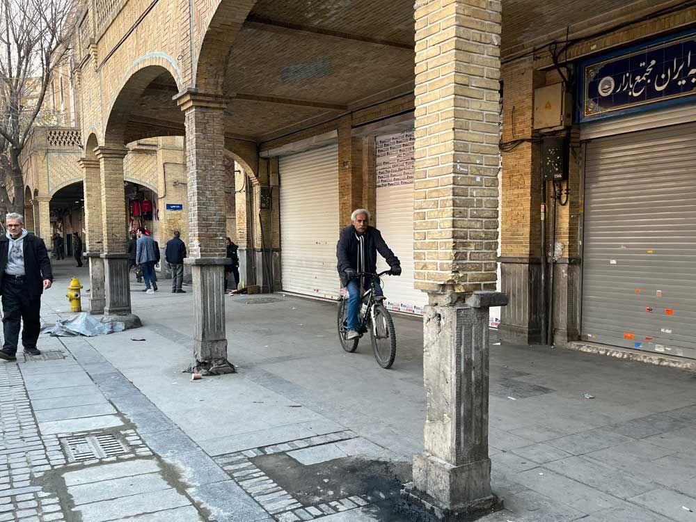A man rides his bicycle as the others walk while shops are closed during protests in Tehran's centuries-old main bazaar, Iran, Tuesday, Jan. 6, 2026.