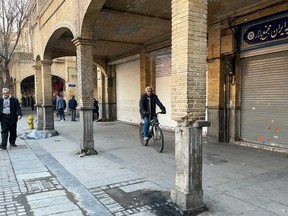 A man rides his bicycle as the others walk while shops are closed during protests in Tehran's centuries-old main bazaar, Iran, Tuesday, Jan. 6, 2026.