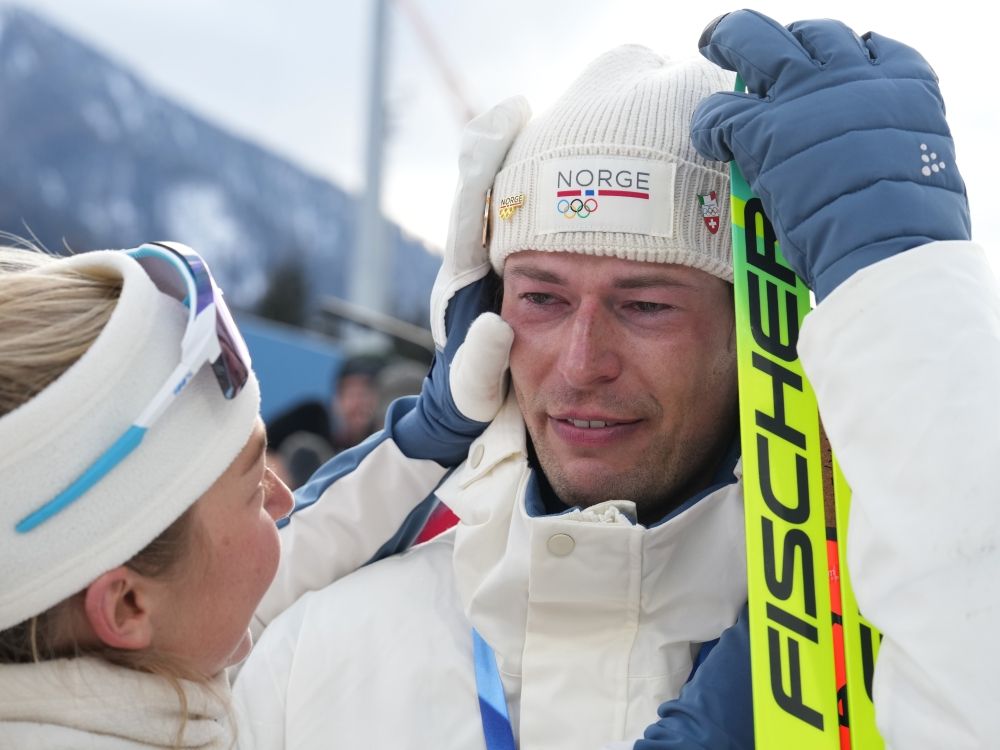 Sturla Holm Laegreid, of Norway, reacts after he won bronze as teammate Ingrid Landmark Tandrevold comforts him after the men's 20-kilometer individual biathlon race at the 2026 Winter Olympics.