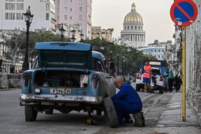 A man tries to repair his old car in a street of Havana.