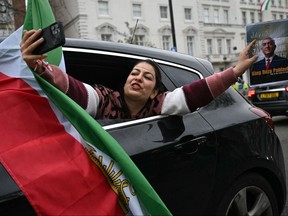 A woman takes a selfie photo while holding a photo of Iranian opposition figure and son of the last Shah of Iran, Reza Pahlav during a drive-by celebration outside the Iranian Embassy in central London, on March 1, 2026.