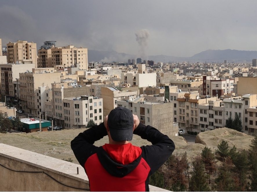  A man looks through biculars as a plume of smoke rises after a military strike on the capital Tehran on March 2, 2026.
