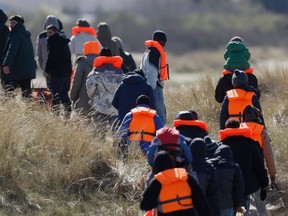 Migrants trying to reach Britain, walk on a beach shore in Gravelines, northern France, Wednesday, March 18, 2026.