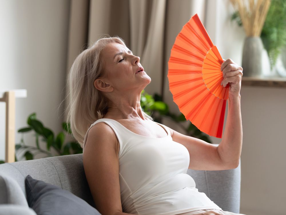 Stressed old woman waving fan suffer from overheating at home
