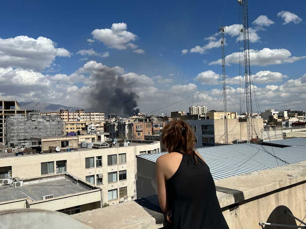  A person watches as plumes of smoke rise over the skyline following explosions on March 1, 2026, in Tehran, Iran.