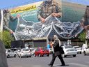 A woman walks past a giant billboard reading 'The Strait of Hormuz remains closed' at the Revolution Square in Tehran on April 12, 2026.