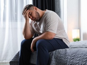 A sad man sits on a bed at home
