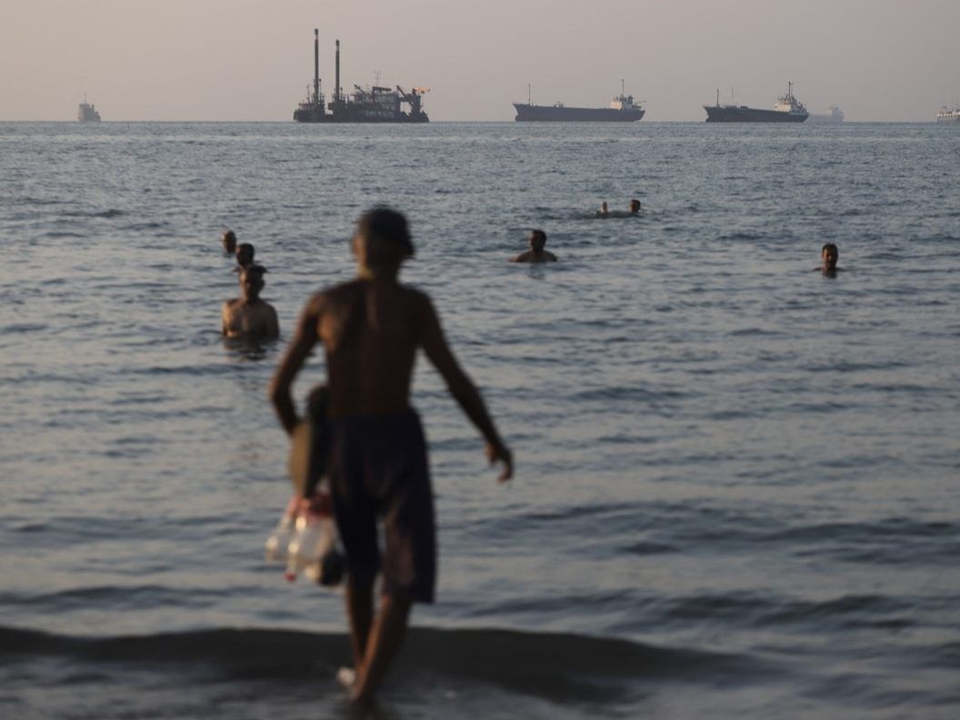 In this picture obtained from Iran's ISNA news agency on June 8, 2026, residents take a dip as cargo and commercial vessels lie at anchor in the Strait of Hormuz off Bandar Abbas. 