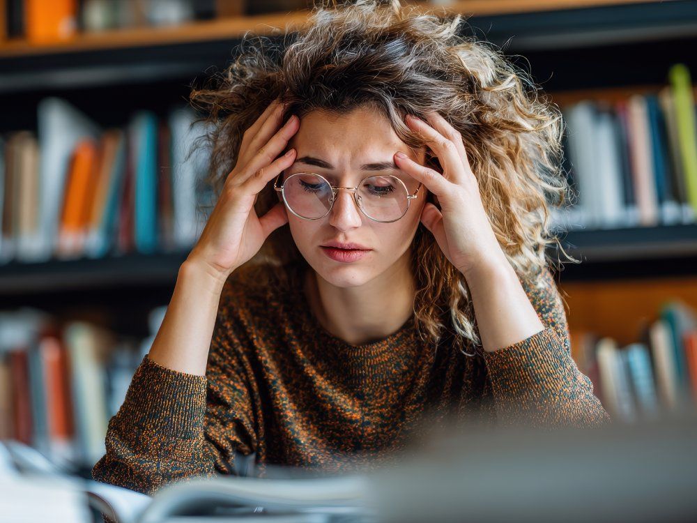 Female student experiencing stress in the library overwhelmed by academic pressures and research assignments leading to anxiety and burnout