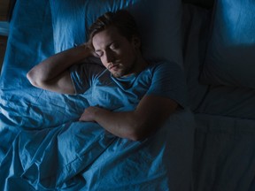 מבט מלמעלה של צעיר יפה תואר ישן בנוחות על מיטה בחדר השינה שלו בלילה. צבעי לילה כחולים עם אור עמוד תאורה חלש קר מבעד לחלון.