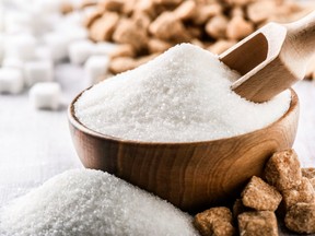 White sugar in wooden bowl with scoop on white table. White and brown sugar cubes in background.