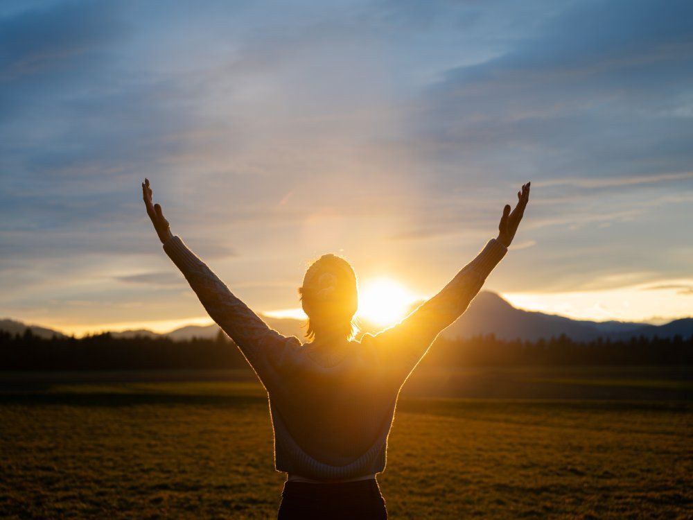 Woman embracing life standing outside in beautiful meadow with her arms raised high
