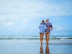 Senior couple walking on the beach holding hands at beach sunrise in evening.
