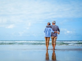 Senior couple walking on the beach holding hands at beach sunrise in evening.
